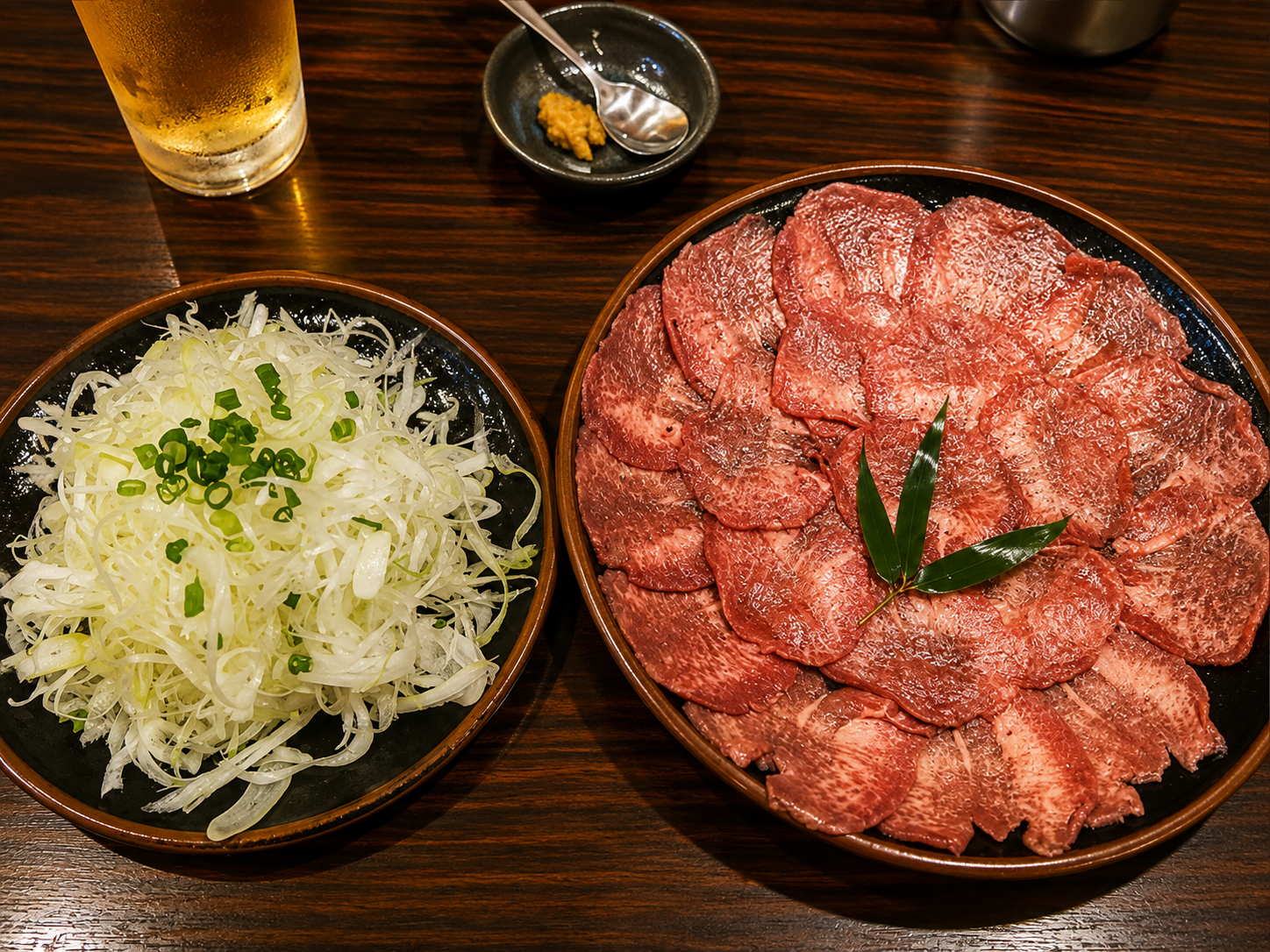 薄切りの牛たんを丸い器に並べたものと、白髪ねぎを山盛りにした器、ビールのグラス