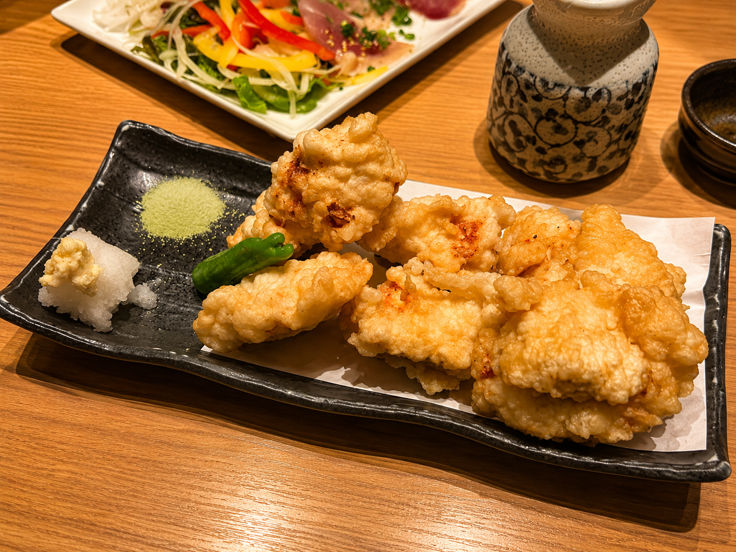 黒い角皿に盛られた鶏の天ぷら。大根おろしと抹茶塩、ししとうが添えられている
