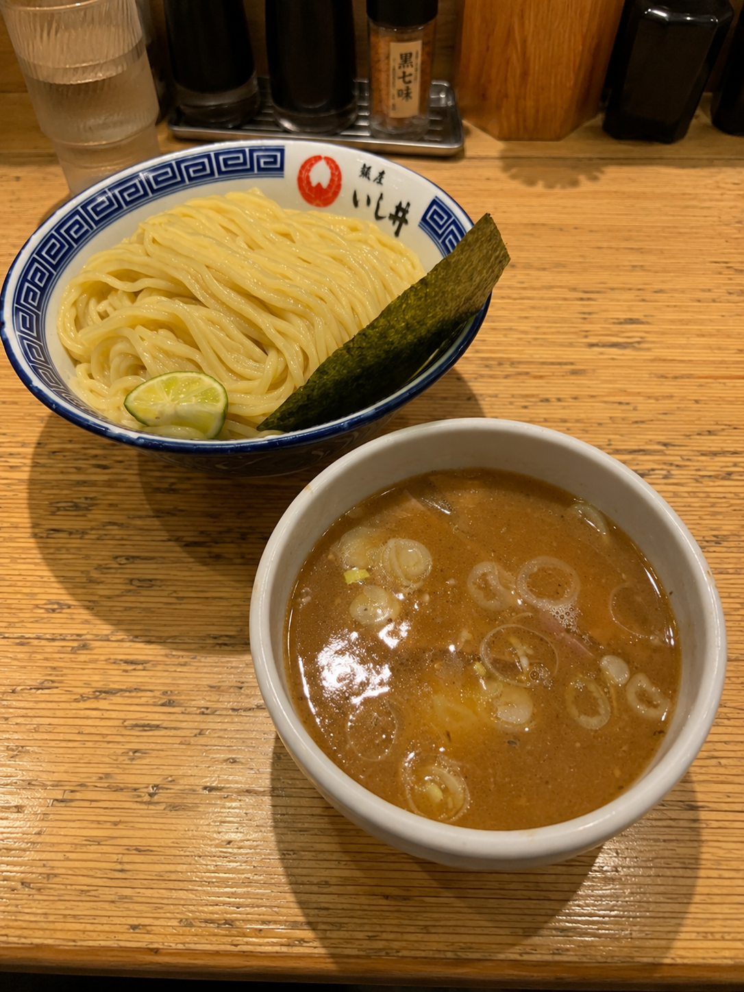 つけ麺。青い縁取りの器に細めのストレート麺、すだちと海苔が添えられ、別の器に濃厚なつけ汁と刻みねぎが入っている