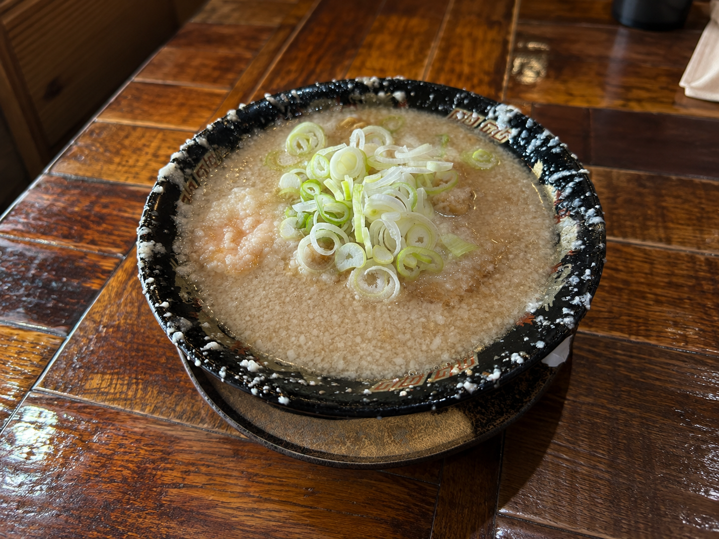 黒い丼に盛られたラーメン。背脂が一面にびっしり浮いた白濁スープに、刻みねぎが乗っている
