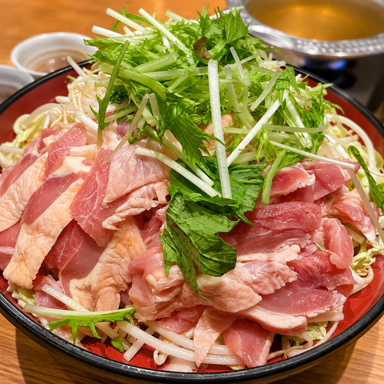 赤い器に薩摩軍鶏の薄切り肉が広げられ、水菜がたっぷり乗っている
