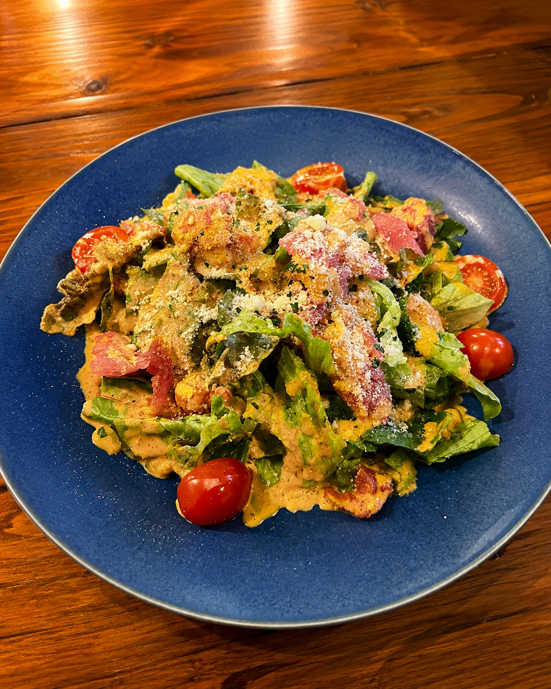 青い皿に盛られた、葉野菜と生ハムをクリームソースで和えた一皿。ミニトマトが添えられている