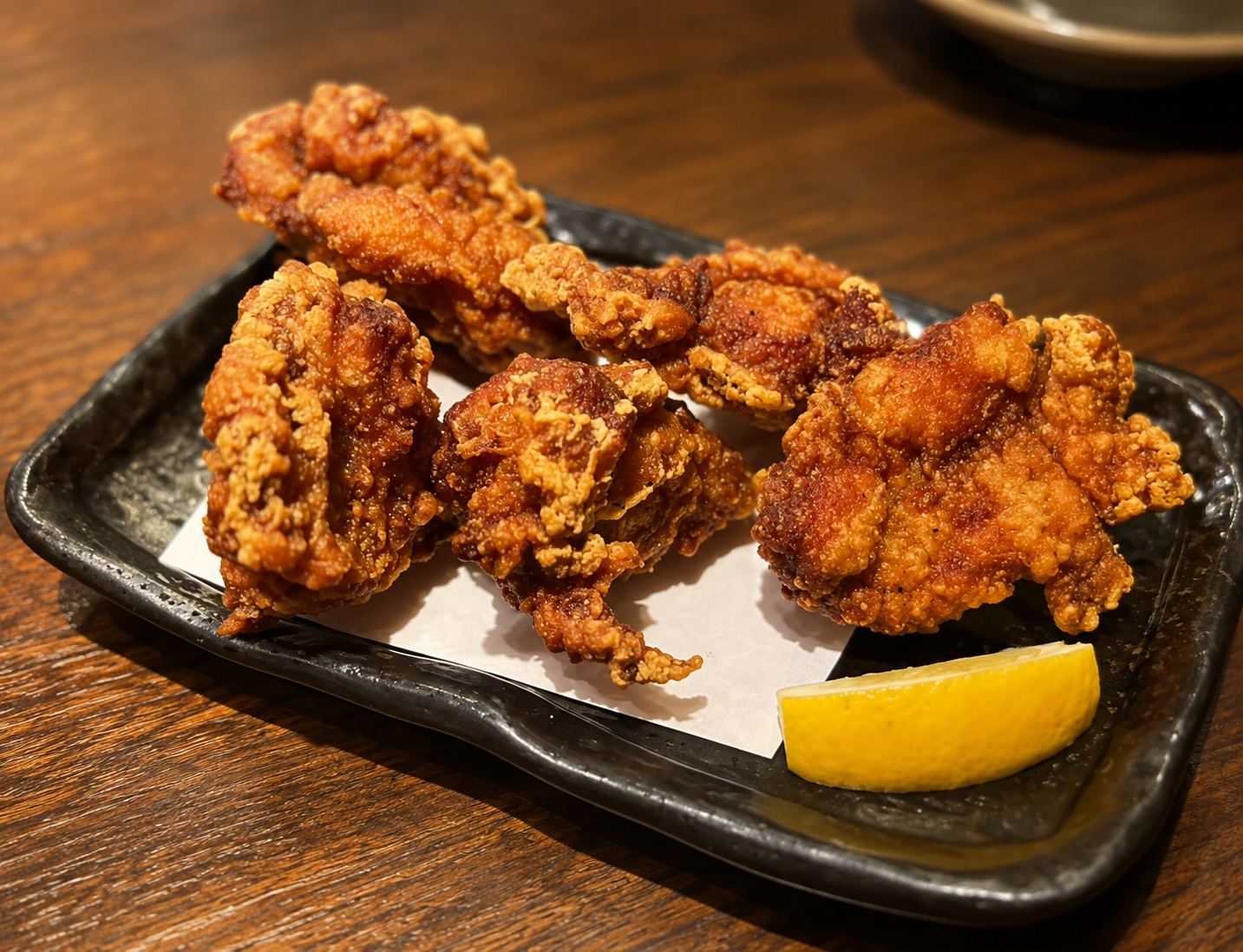 黒い角皿に盛られた鶏の唐揚げ4個とレモン