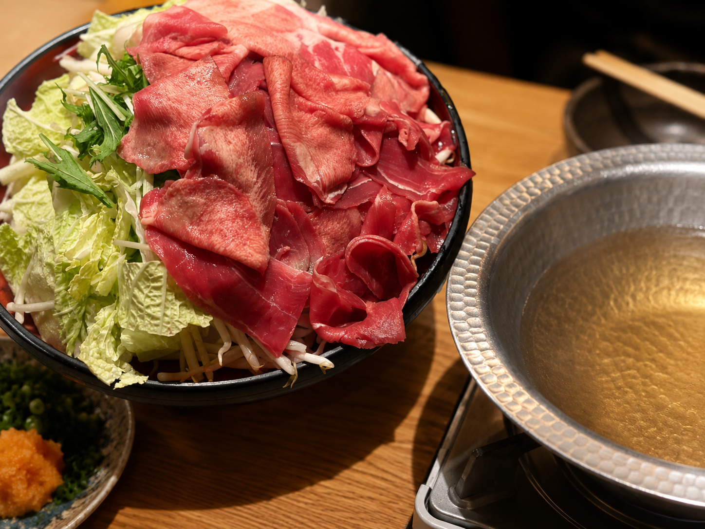 しゃぶしゃぶ用の薄切り肉と白菜・水菜・もやしを盛った器と、出汁の張られた銀色の鍋