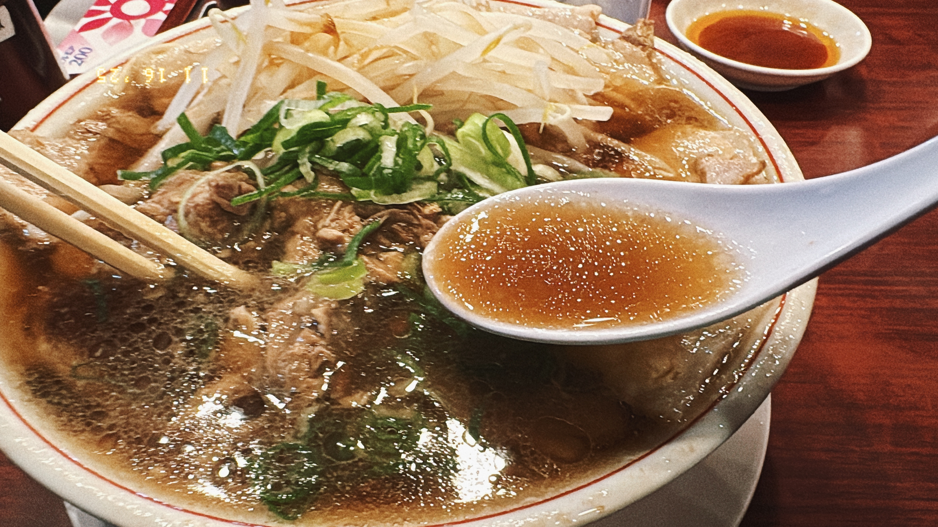 レンゲで醤油スープをすくっている様子。透明感のある茶色いスープ