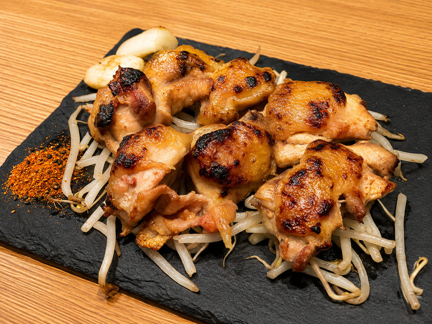 黒いスレート皿に炭火で焼いた鶏肉が並び、もやしと一味唐辛子が添えられている