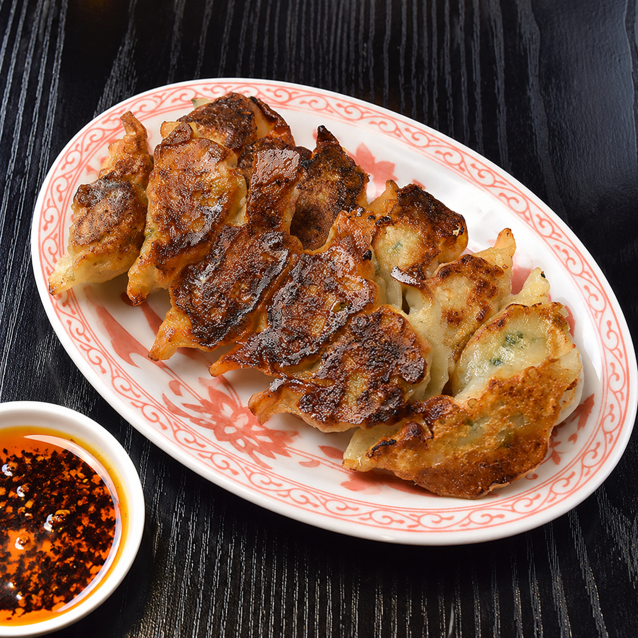 焼き目のついた餃子が楕円の皿に盛られ、ラー油の入った小皿が添えられている