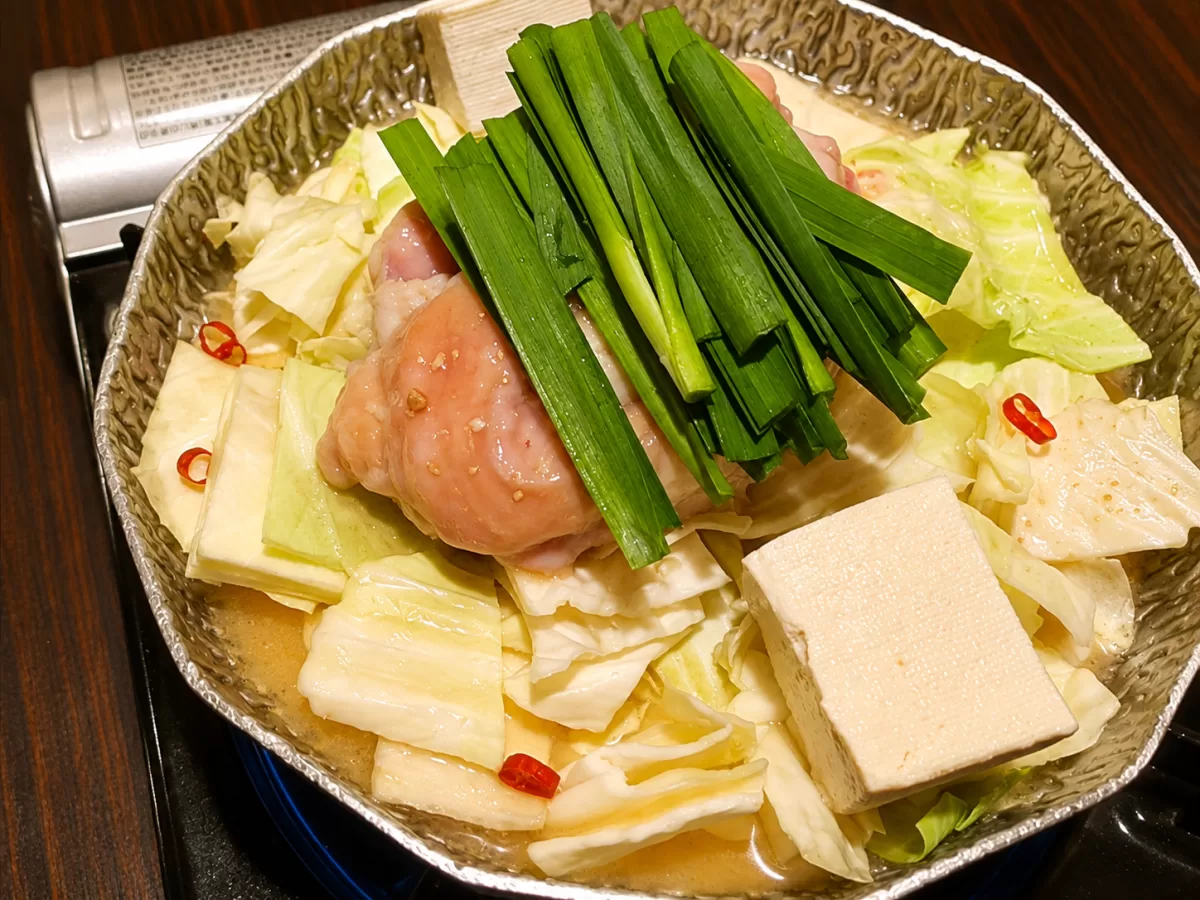銀色の鍋に鶏肉・キャベツ・豆腐・ニラ・赤唐辛子を入れて煮込んでいる